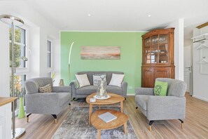 Ein Wohnzimmer mit zwei grauen Sesseln, einem runden Couchtisch und einer Vitrine mit Glastüren.