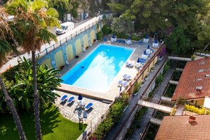 Ein Pool mit Liegestühlen und Sonnenschirmen, umgeben von Grünflächen und Gebäuden.