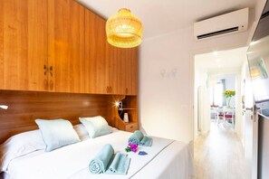 Ein Hotelzimmer mit Holz-Kopfteil, einem Bett mit weißer Bettwäsche, einem gerollten Handtuch, einem kleinen Nachttisch und einer hängenden Leuchte.