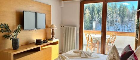 Ett hotellrum med en säng, ett skrivbord, en tv och utsikt över ett snötäckt landskap.