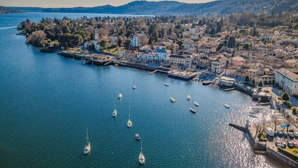 An aerial view of a coastal town with a marina, boats, and buildings along the waterfront. - A Ca` di Chiara e Fabio - Panoramica Lago Maggiore (Lesa)