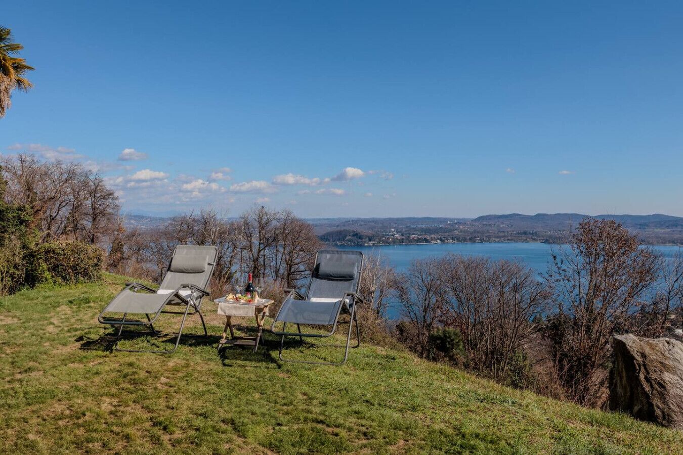 Zona verdeggiante con sedie a sdraio e un tavolo, con vista su un lago e una cittadina in lontananza.