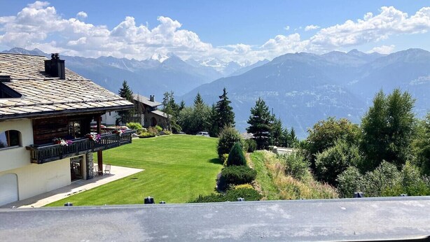 A mountain view with a building featuring a balcony and a lawn.