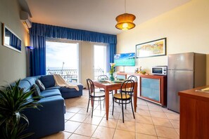 Ein Wohnzimmer mit Sofa, Esstisch, Stühlen, einem Fernseher und einer Küchenzeile mit Kühlschrank.