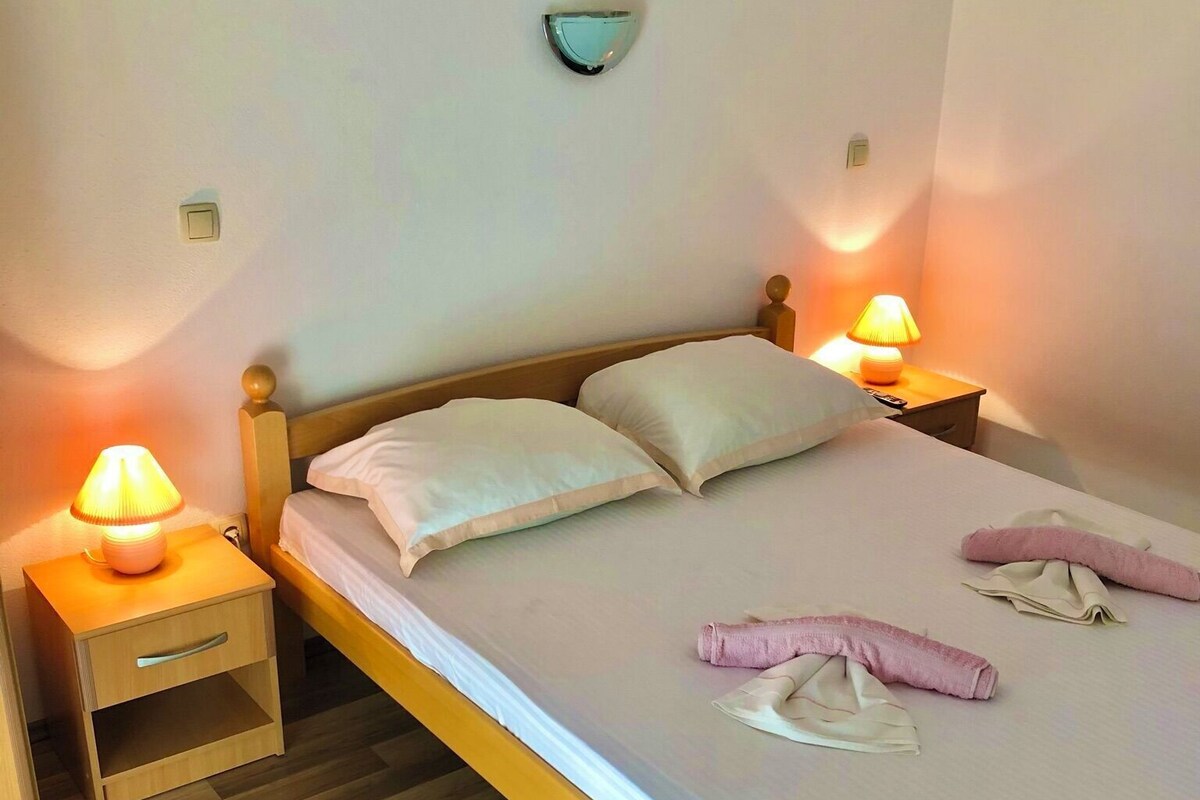 A bed with two pillows, a bedside table with a lamp, and a wall-mounted light fixture.
