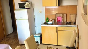 A compact kitchen with a refrigerator, microwave, sink, and stove. There is a dining table with chairs and a vase of flowers. - Apartments Luka (Omis)