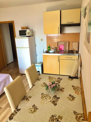 A compact kitchen with a refrigerator, microwave, sink, and stove. There is a dining table with chairs and a vase of flowers. - Apartments Luka (Omis)