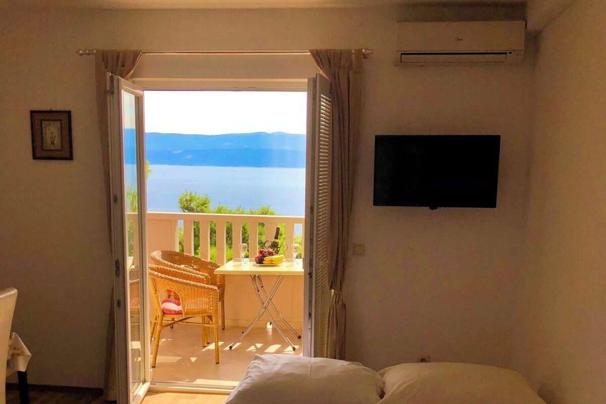 A hotel room with a bed, a TV, a balcony with a view of the sea, and a chair.