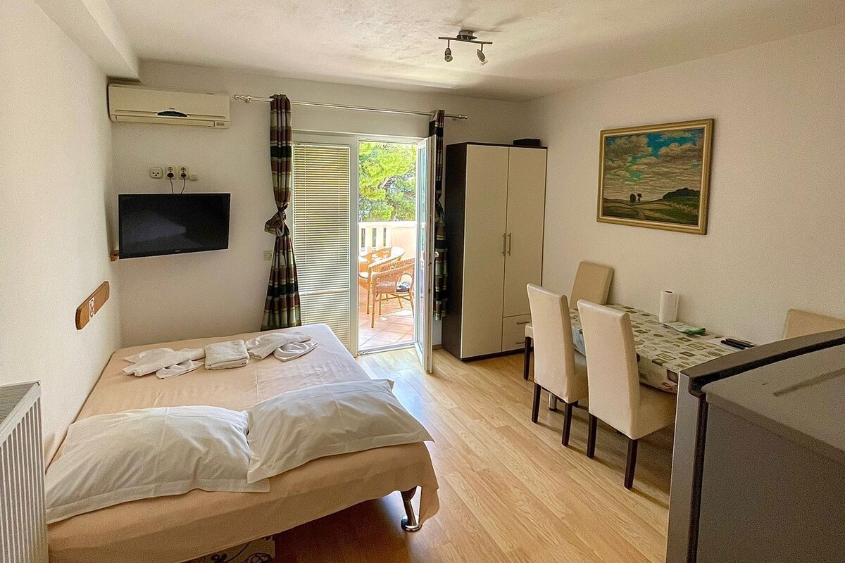 A bedroom with a bed, a desk, a chair, a TV, and a painting.