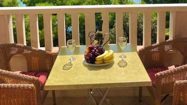 A table with a bottle of champagne, a fruit platter, and two glasses on a balcony overlooking a body of water and distant mountains. - Apartments Luka (Omis)