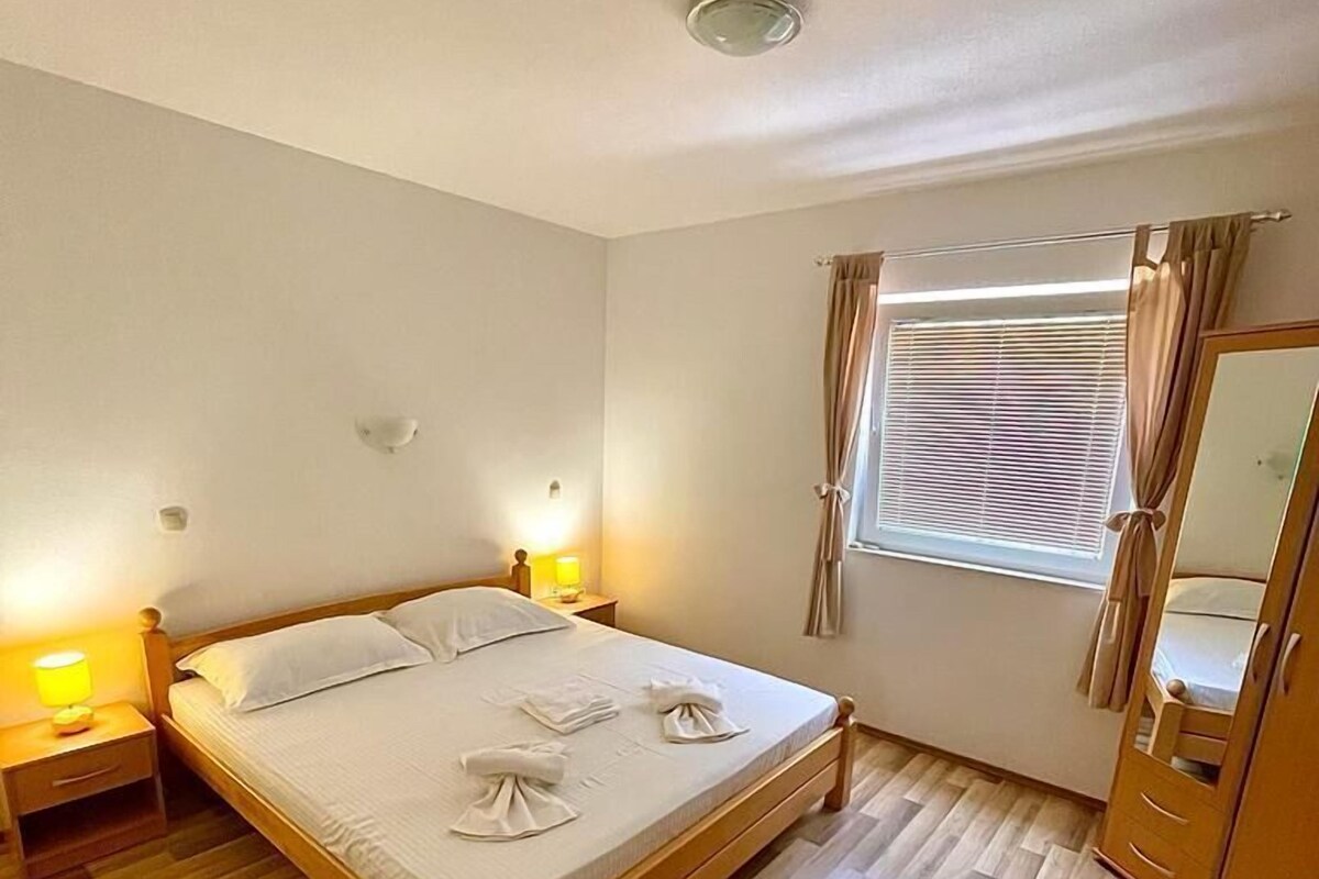 A bedroom with a wooden bed, bedside lamps, a window with blinds, and a mirror.