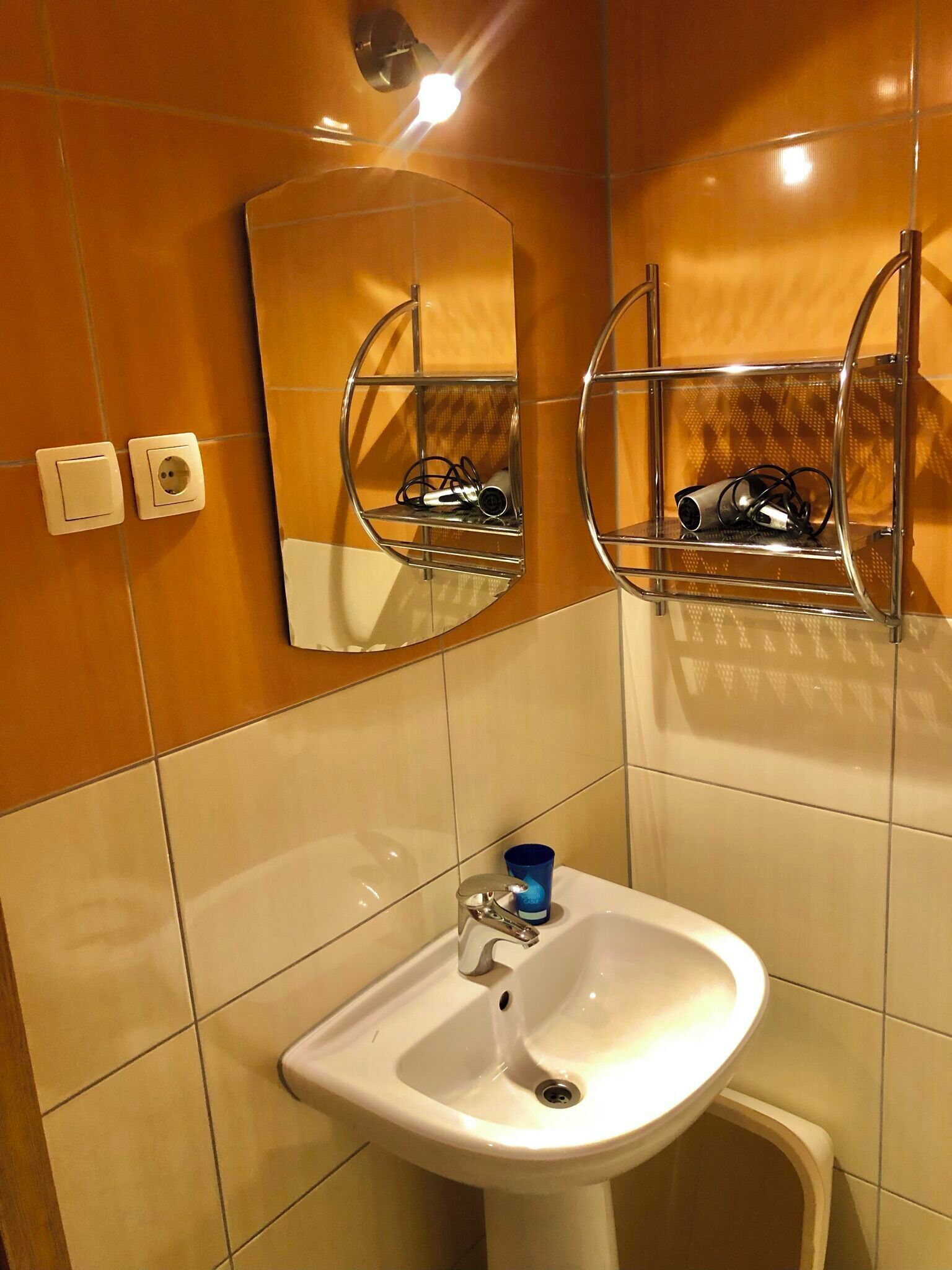 A bathroom with a white sink, a mirror, and a shelf with a camera.