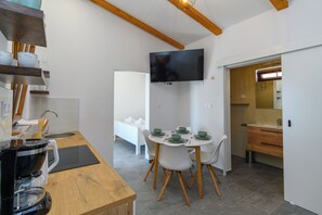 A modern kitchen with a dining area, a TV mounted on the wall, and a wooden ceiling. - House Guesthouse Stipe (Lopar)