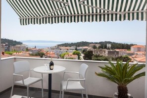 A balcony with a striped awning, two white chairs, a table with a bottle and glass, and a potted plant. - Apartment Town and Beach (Makarska)
