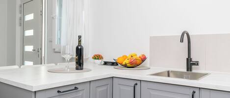 Una cuina moderna amb taulell blanc, rentamigles d'acer inoxidable i armaris grisos.