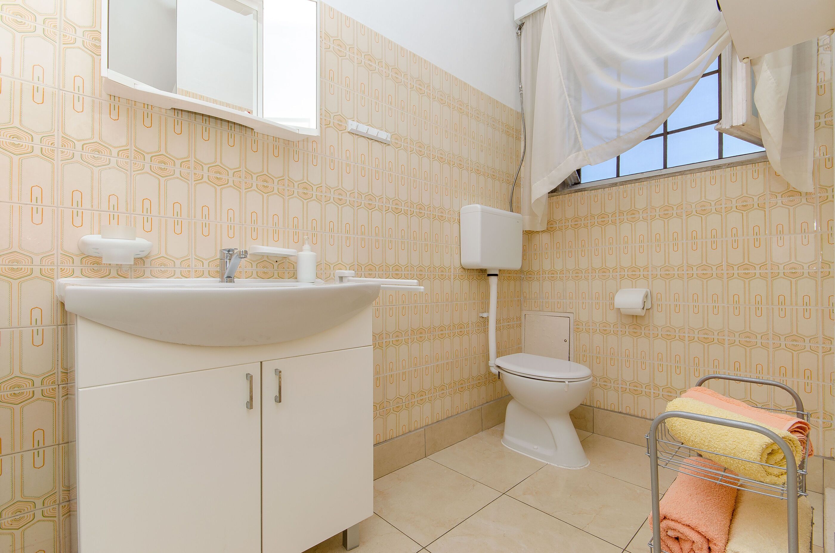 A bathroom with a sink, toilet, and a window with curtains.