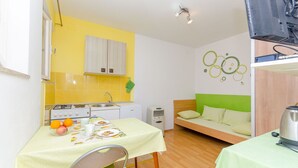 A compact room with a kitchenette, a dining table with a green tablecloth, a sofa with green cushions, and a wall-mounted television. - Apartment Green Rustic (Split)