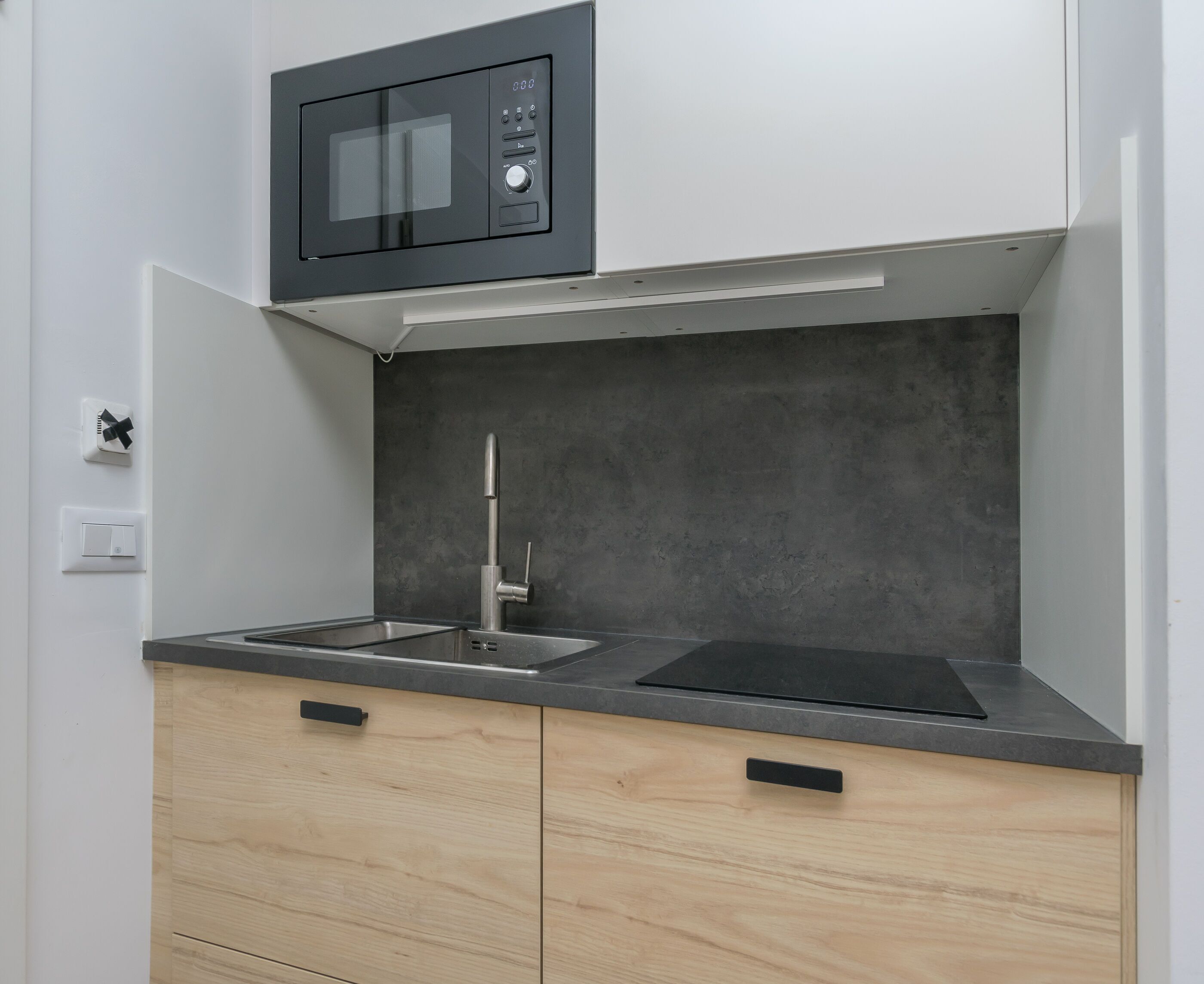 A modern kitchen with a built-in microwave, a stainless steel faucet, and wooden cabinets.