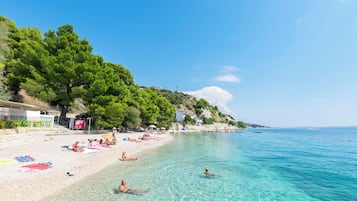 Una playa con agua cristalina, gente tomando el sol y algunas embarcaciones.
