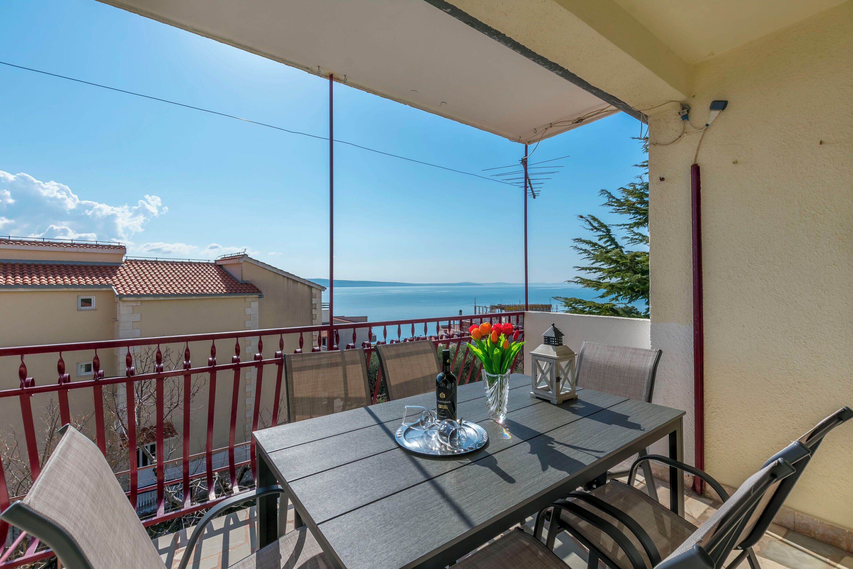 A balcony with a table, chairs, a vase with flowers, a bottle, and a tray.