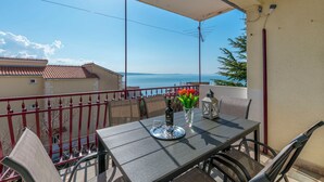 A balcony with a table, chairs, a vase with flowers, a bottle, and a tray. - Apartment Jadran (Omis)