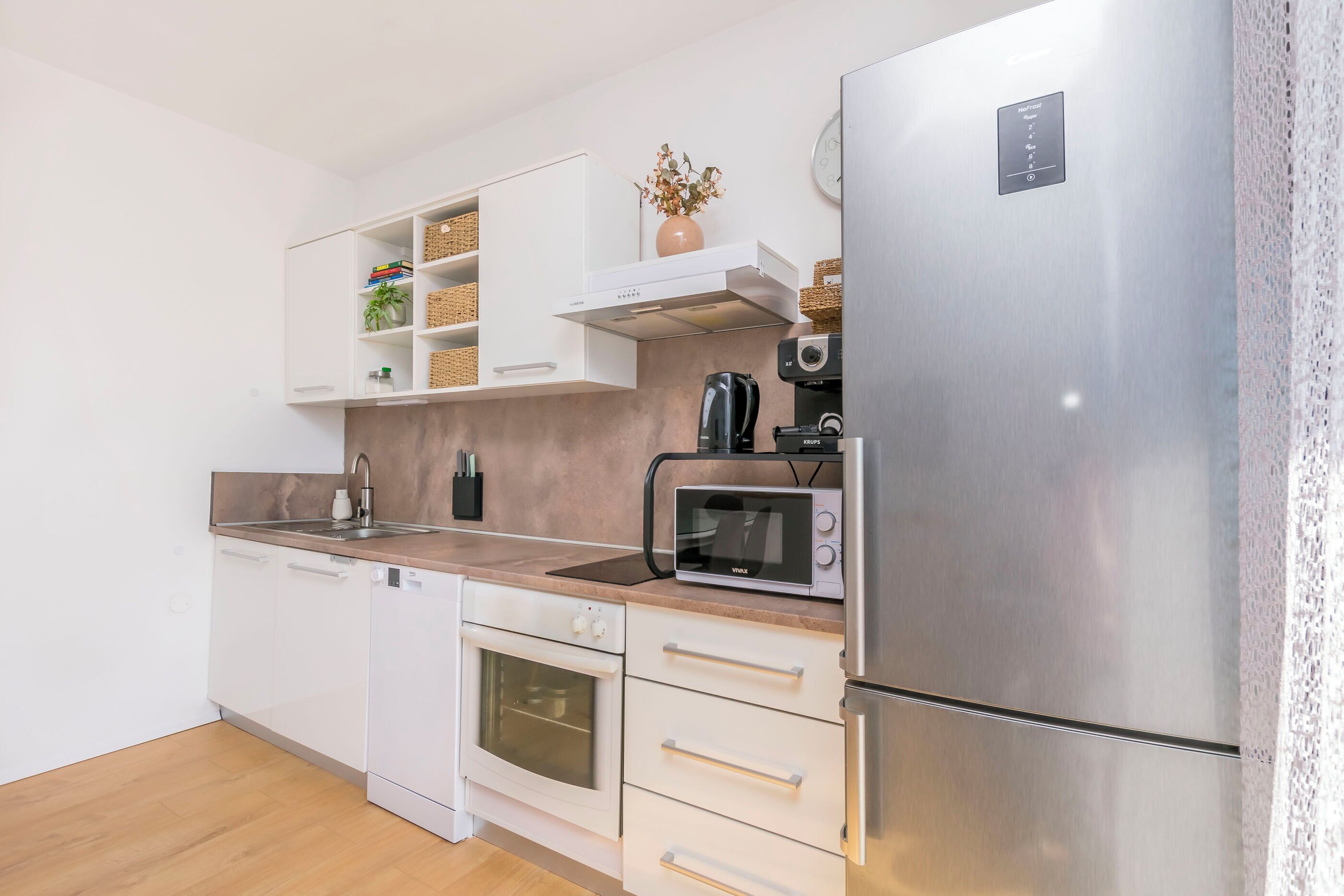 A modern kitchen with white cabinetry, a stainless steel refrigerator, a microwave, and a built-in oven.