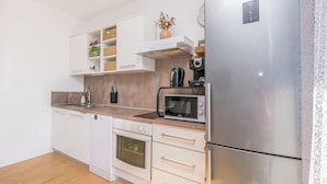 A modern kitchen with white cabinetry, a stainless steel refrigerator, a microwave, and a built-in oven. - Apartment Jadran (Omis)