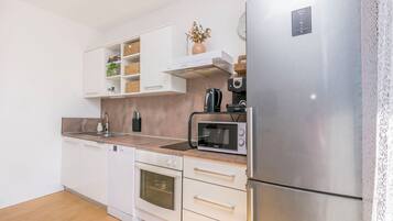 Una cocina moderna con armarios blancos, un refrigerador de acero inoxidable, un microondas y un horno empotrado.
