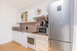 A modern kitchen with white cabinetry, a stainless steel refrigerator, a microwave, and a built-in oven. - Apartment Jadran (Omis)