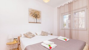 A double bed with a pink bedspread, two white pillows, a nightstand with a lamp, and a painting of trees on the wall. - Apartment Jadran (Omis)