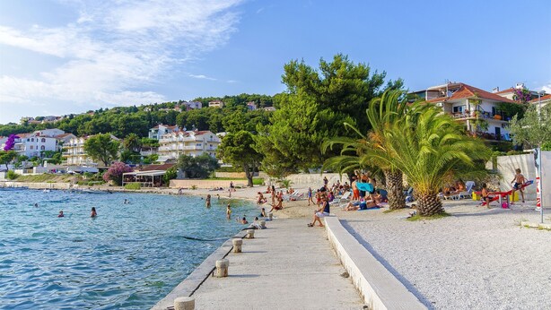 A coastal scene with a beach, swimming people, and buildings in the background. - Apartment Sunset 3 (Trogir)
