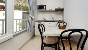 Een kleine keuken met een magnetron, waterkoker en een tafel met stoelen.