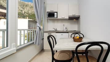 Uma cozinha compacta com micro-ondas, chaleira e uma mesa com cadeiras.