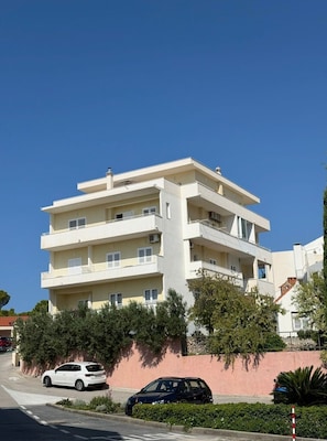 A multi-story building with balconies, a parking area, and a clear sky. - Apartments Cvita (Igrane)