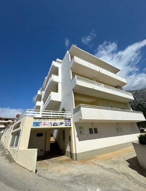 A multi-story building with balconies, a sign indicating 'APARTMANT LULIC,' and a clear blue sky in the background. - Apartments Cvita (Igrane)