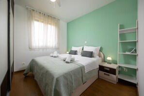 A bedroom with a bed, nightstands, a bedside table with a lamp, a shelf, and a window with curtains. - Apartment Znjan Park and Stay (Split)
