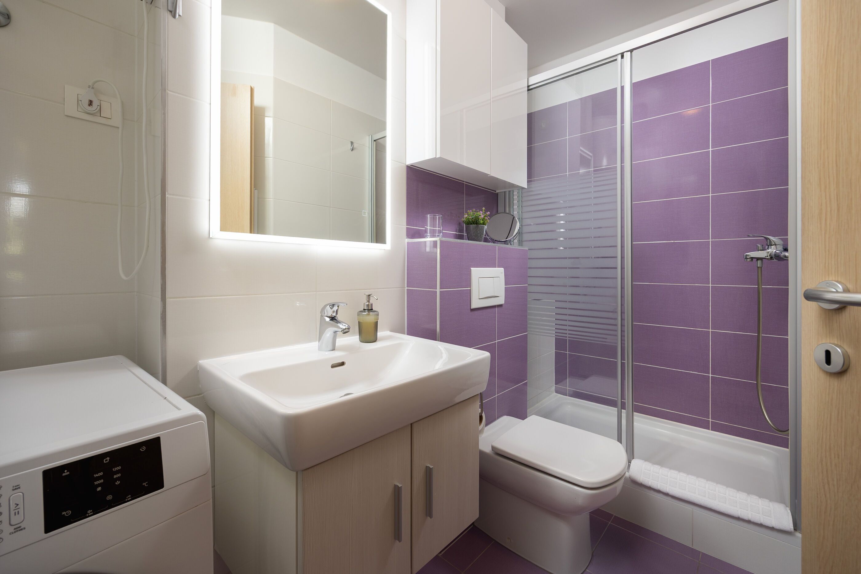 A bathroom with a white sink, a toilet, and a shower with purple tiles.