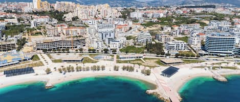 An aerial view of a coastal city with residential buildings, a beach, and clear blue waters.