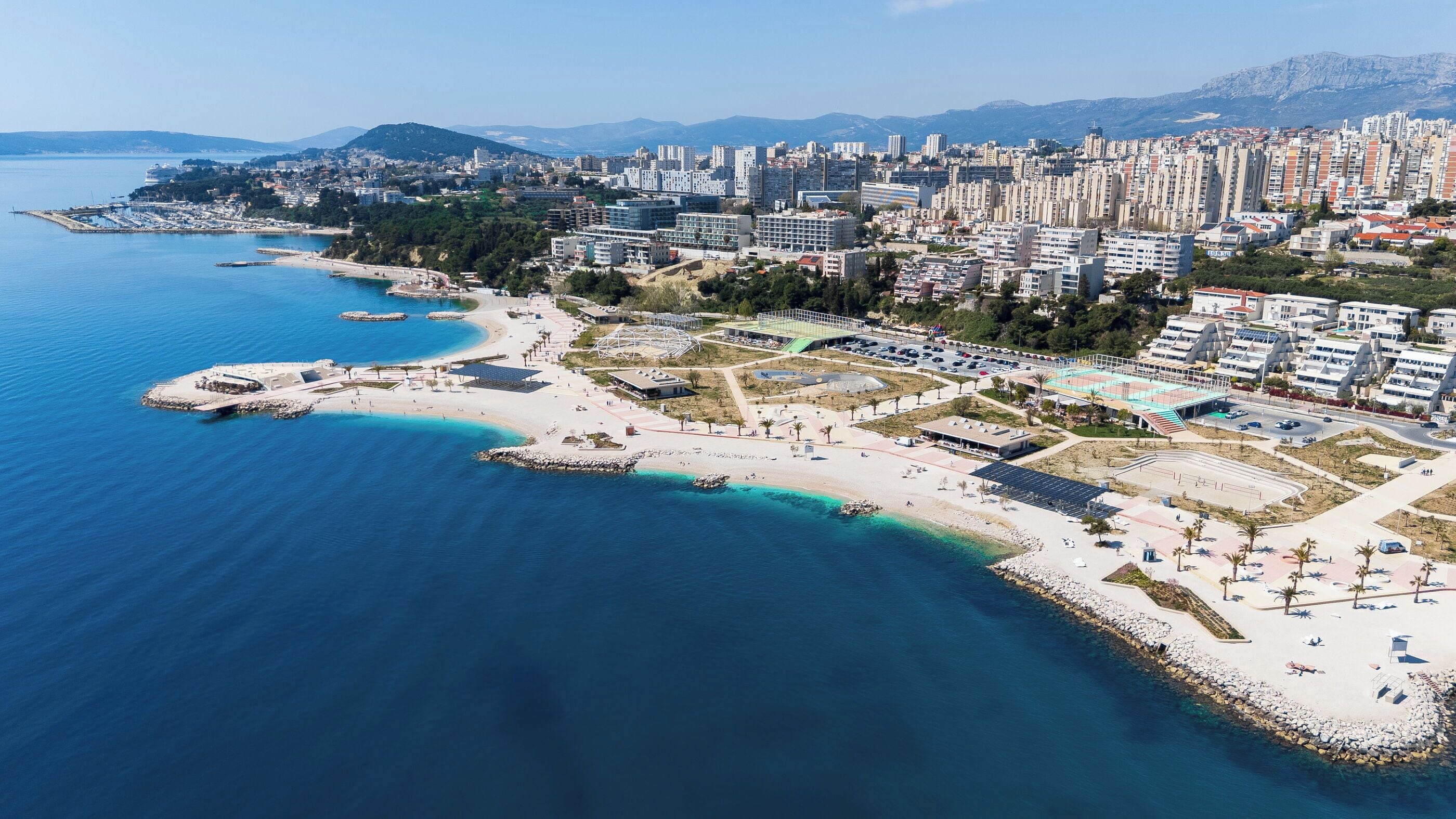 An aerial view of a coastal city with a marina, beach, and high-rise buildings.