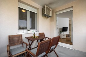 A balcony with a table and chairs, a window with blinds, a wall-mounted air conditioner, and a television in the adjacent room. - Apartment Znjan Park and Stay (Split)