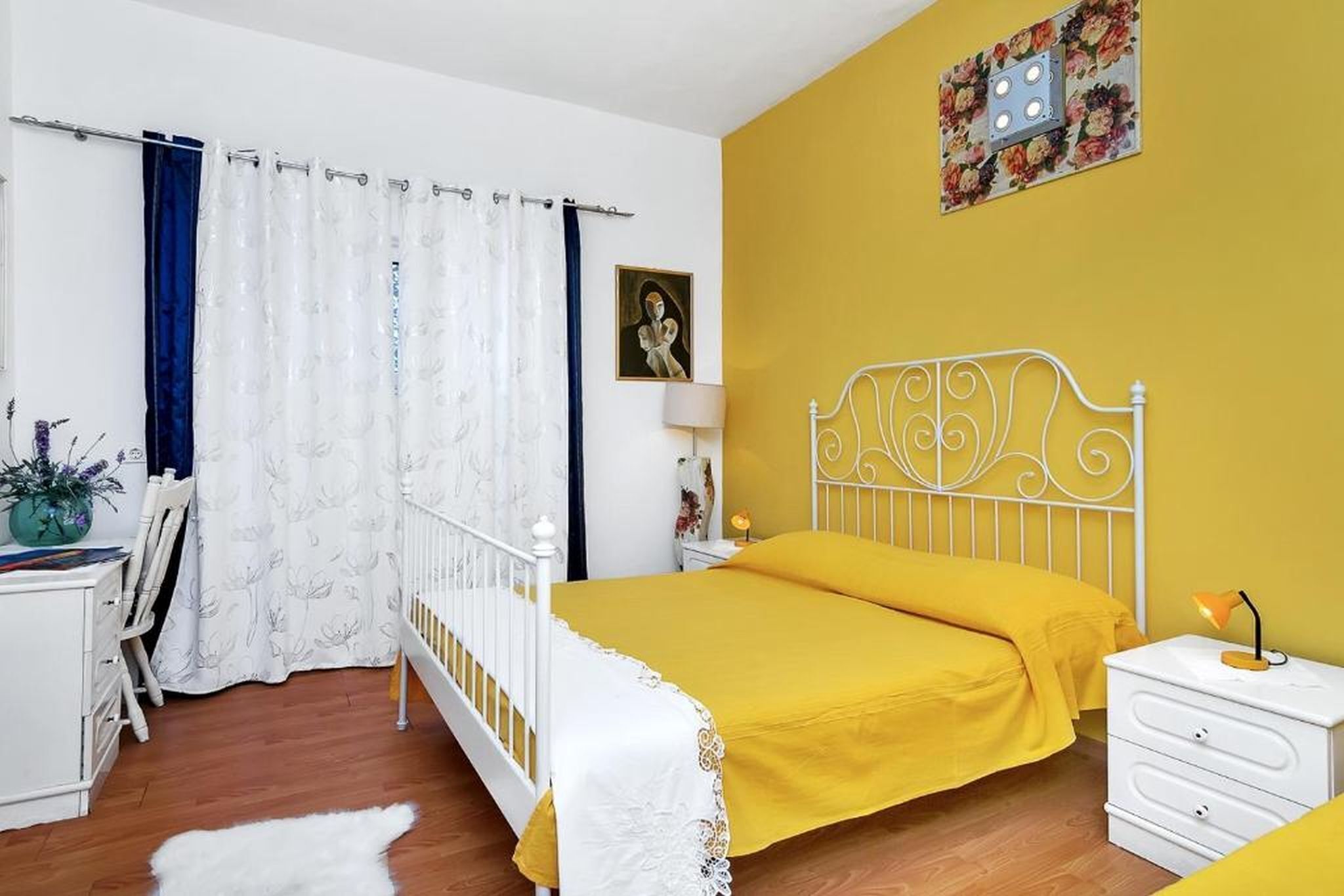 Une chambre à coucher avec un lit, une table de chevet, une chaise, un bureau, une lampe, un tableau au mur et un rideau.