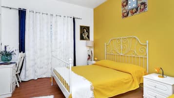 Une chambre à coucher avec un lit, une table de chevet, une chaise, un bureau, une lampe, un tableau au mur et un rideau.