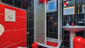 Un baño con paredes revestidas de baldosas negras y rojas, un lavamanos blanco y un cubo de basura rojo.
