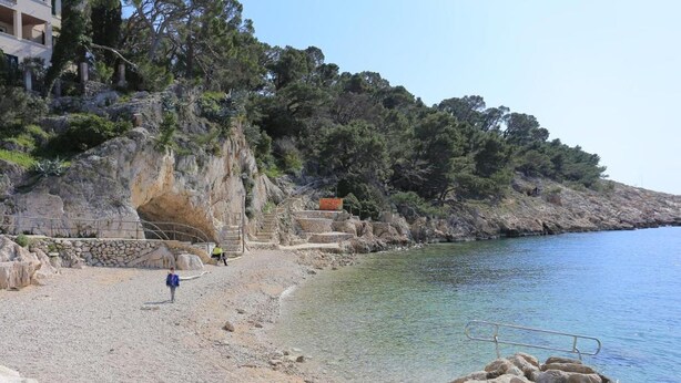 Una spiaggia rocciosa con delle scale che scendono verso l'acqua, una ringhiera e un edificio sullo sfondo.