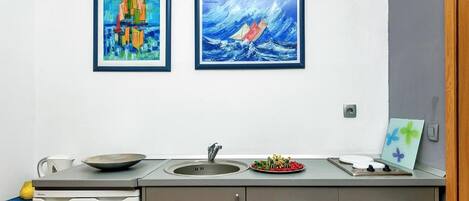 A kitchen with a sink, a stove, and a countertop. There are two framed paintings on the wall.