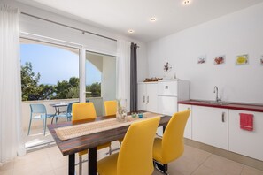 A modern kitchen with a dining area, a balcony with chairs, and a view of the outdoors. - Apartments White House (Marusici)