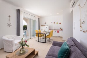 A modern living room with a sofa, a dining table with chairs, a white armchair, and a glass door leading to an outdoor area. - Apartments White House (Marusici)