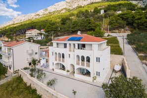 A multi-story building with balconies, a solar panel, and a paved area with plants. - Apartments White House (Marusici)