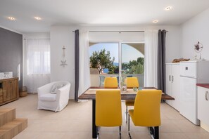 A modern kitchen with a dining area, a white sofa, and a view of the outdoors. - Apartments White House (Marusici)