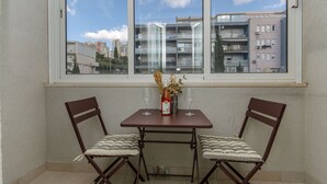 A corner room with a window overlooking a cityscape, a small table with two chairs, and a vase with dried flowers. - Apartment Beachfront Daria (Split)
